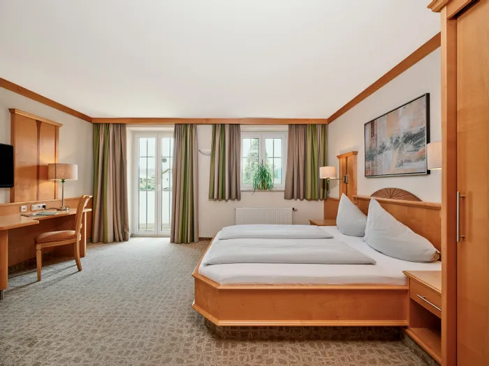 Spacious hotel room with double bed, wooden furniture, desk, and natural light from balcony
